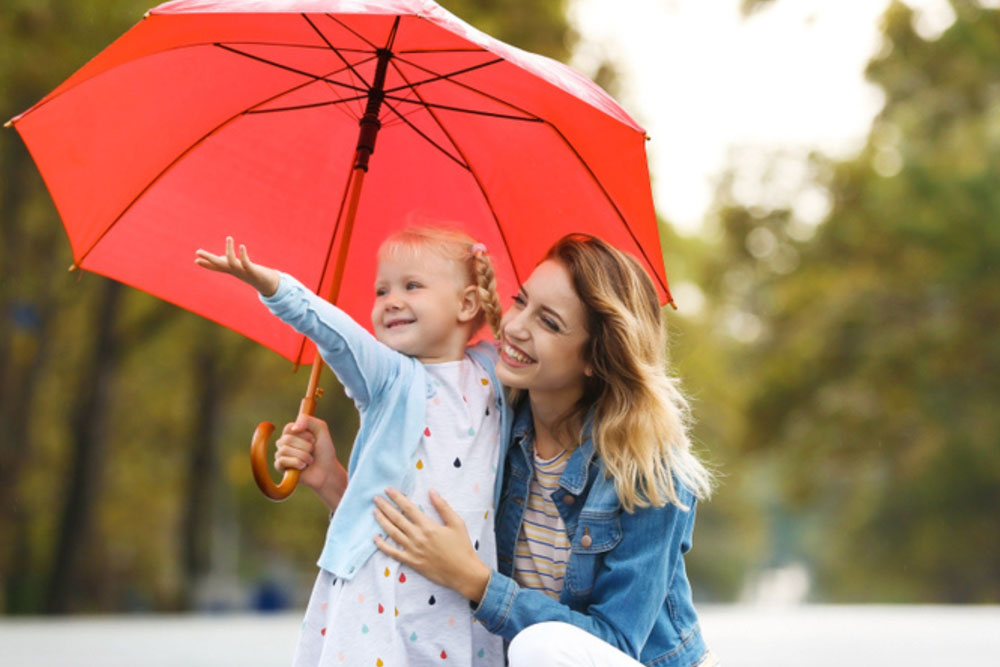 A smiling woman kneels beside a young girl holding a red umbrella - https://www.richardgreeninsurance.com/