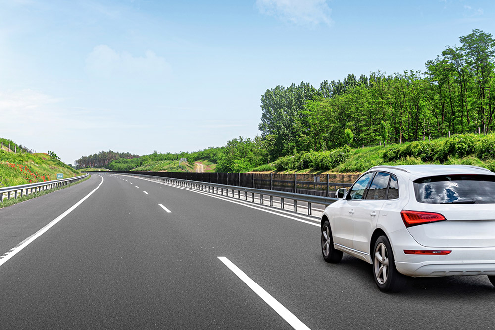 A white SUV drives on an empty highway bordered by lush greenery under a clear blue sky - https://www.richardgreeninsurance.com/