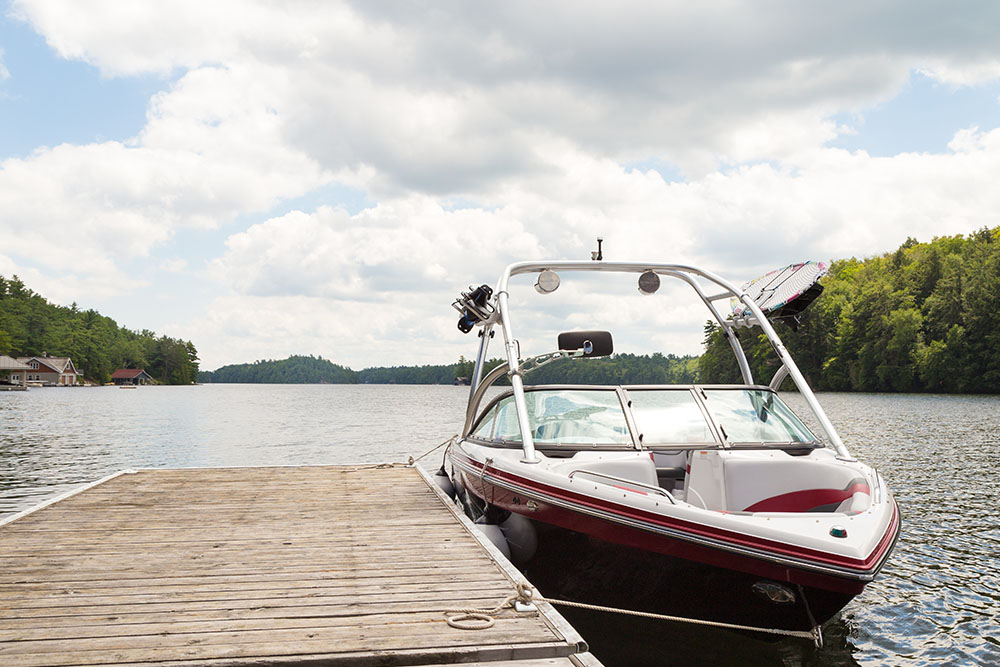 A sleek motorboat is docked next to a wooden pier on a tranquil lake - https://www.richardgreeninsurance.com/