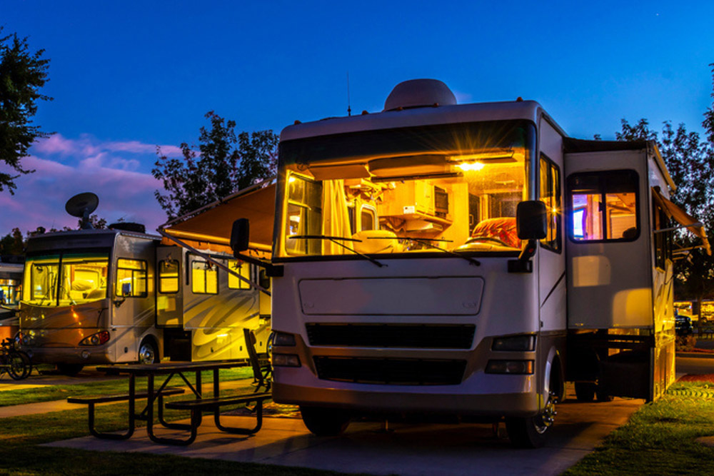 Two RVs parked at a campsite during twilight, warmly lit from within - https://www.richardgreeninsurance.com/