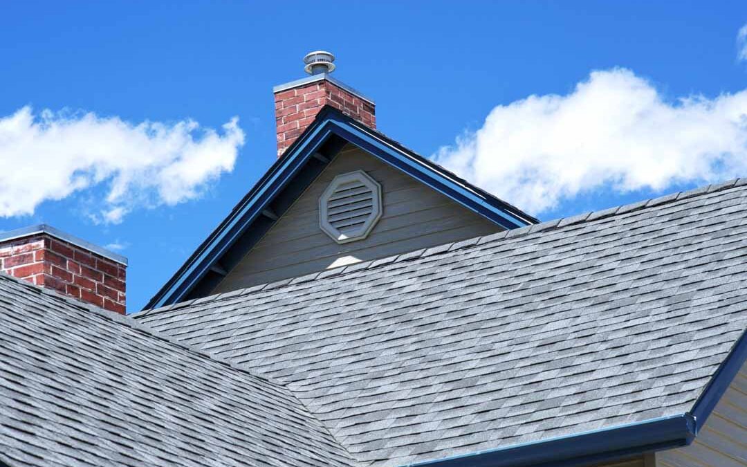 A residential roof featuring a chimney with a protective cap on top, set against a clear blue sky